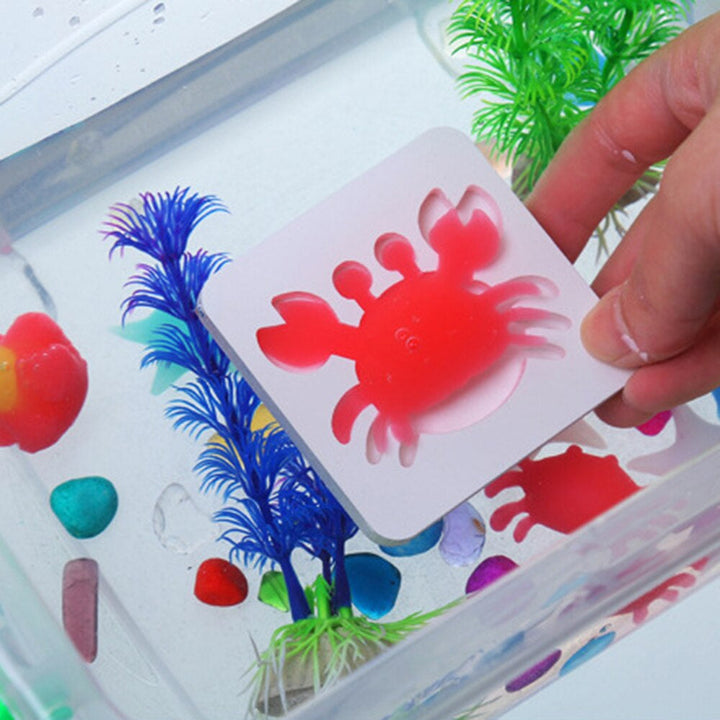 Hand holding a mold with a red crab figure above a water-filled container