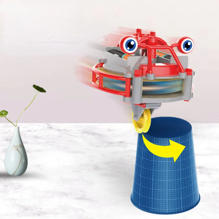 Red balancing robot with its yellow wheel resting on the rim of a blue cup.
