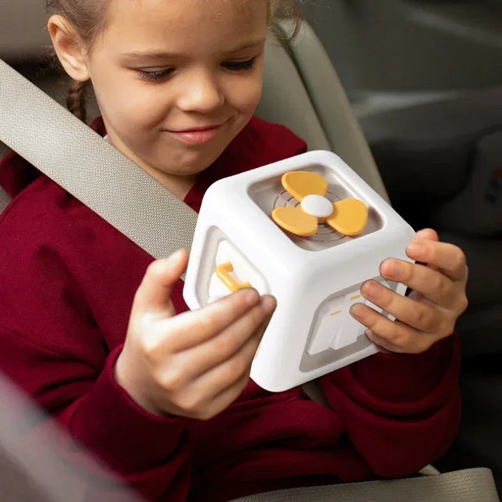 Child holding a white sensory cube with a yellow spinner and moving controls