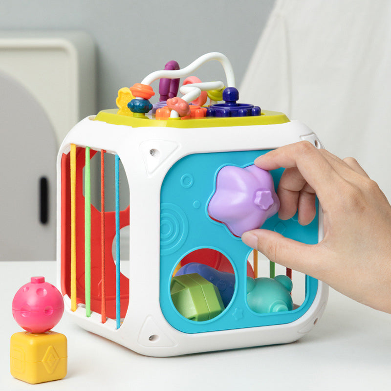 Shape sorter cube with a purple heart piece at the front and yellow and pink pieces beside it