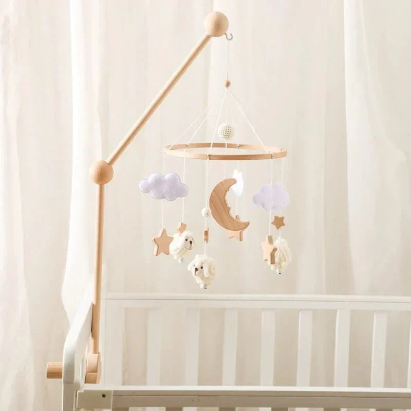 Sheep-and-moon baby mobile hanging from a wooden arm, shown from the side of a crib