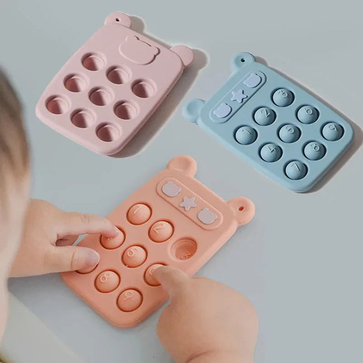 Child pressing the numbered buttons on an orange silicone phone beside pink and blue versions