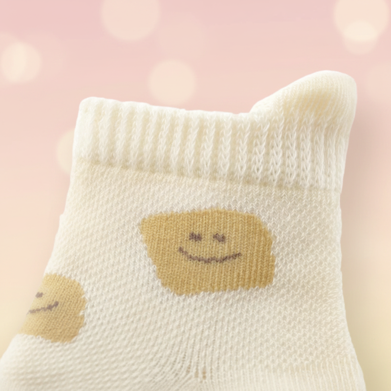 Close-up of a cream smiley-pattern baby sock with a ribbed cuff and open knit texture.