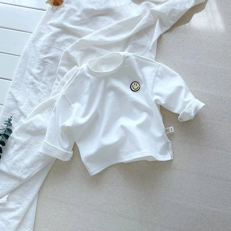 Solid white long-sleeve shirt with a crew neck and a small smile patch.