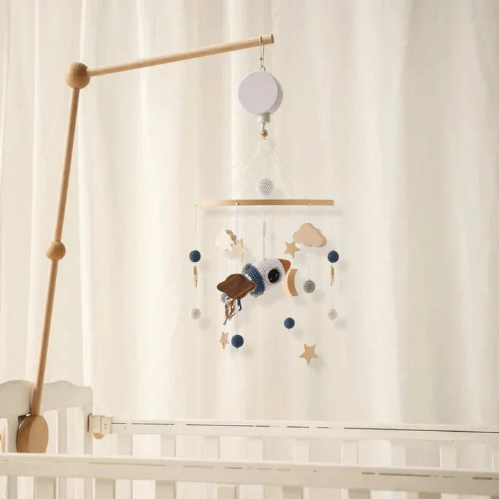 Space baby mobile with a rocket and hanging stars displayed on a wooden arm beside a crib