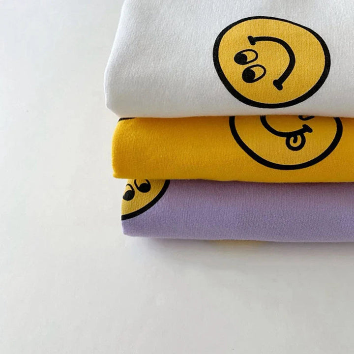 Close-up of stacked white, yellow and purple cotton tops with smiley-face prints