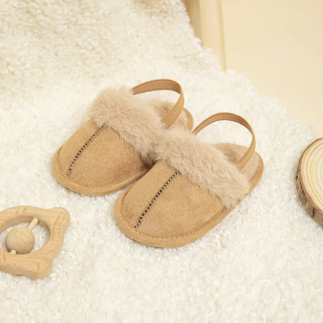 Pair of tan baby slippers with fluffy trim, center stitching and heel straps