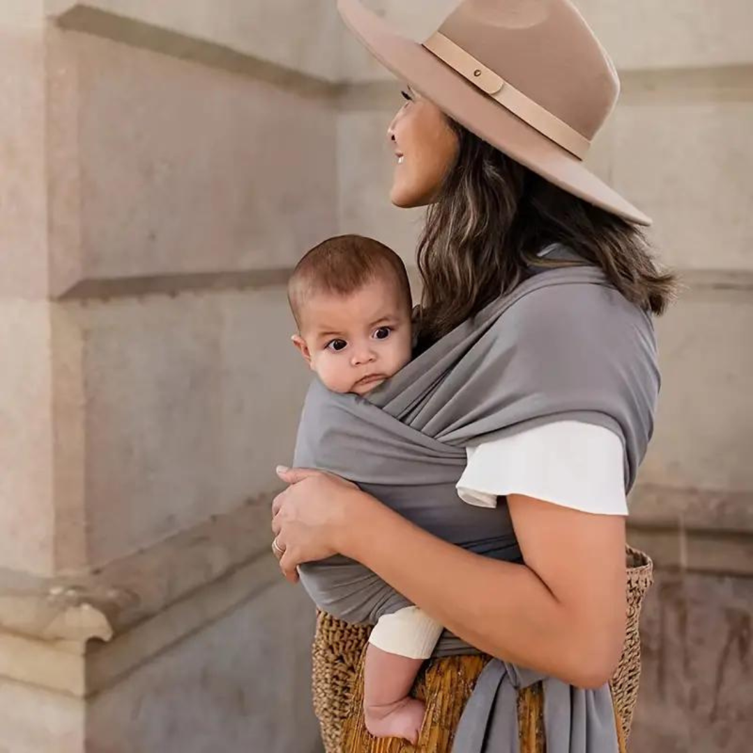 Parent wearing a taupe-gray baby wrap while carrying a baby outdoors