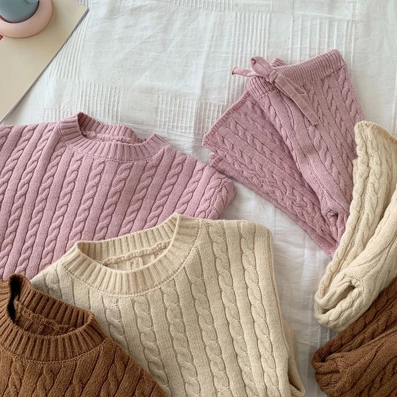 Close-up of pink, beige, and brown cable-knit sweaters with matching knit pants