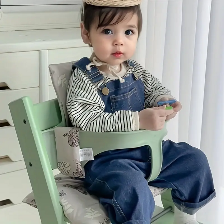 Child seated with a gray tiger-and-leaf cushion in a mint-green high chair