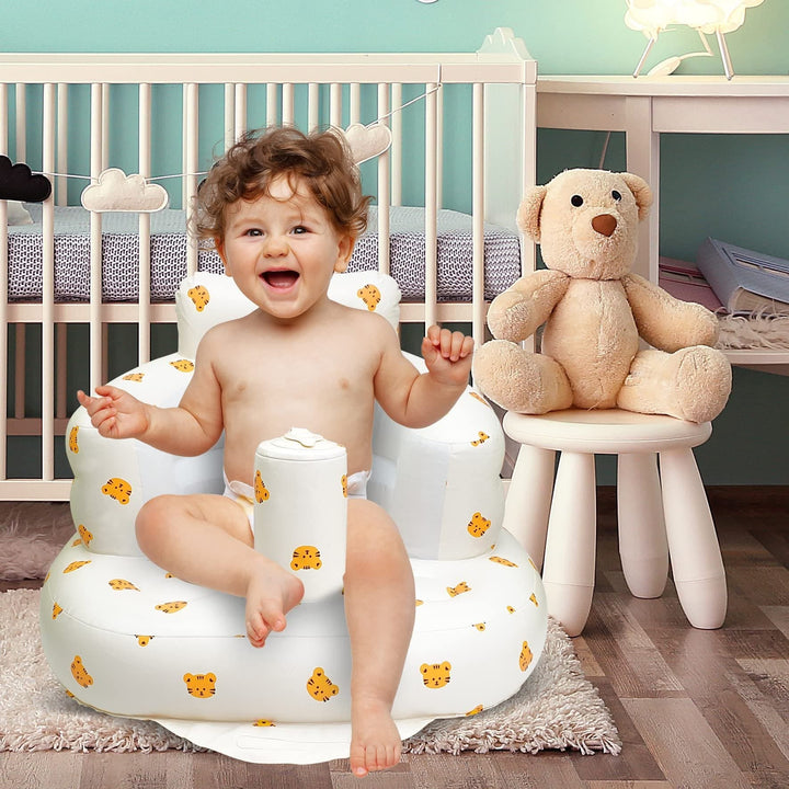 Child sitting in a tiger-print inflatable baby seat beside a crib and teddy bear.