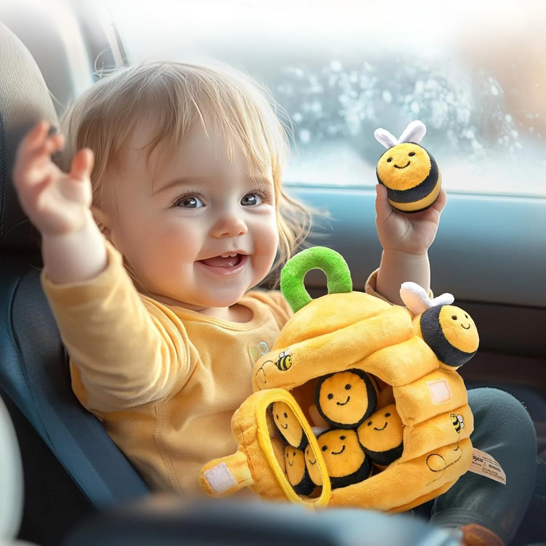 Toddler holding a plush bee beside a yellow beehive toy in a car seat
