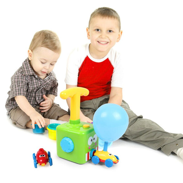 Two children beside a green hand pump and a yellow car with an inflated blue balloon