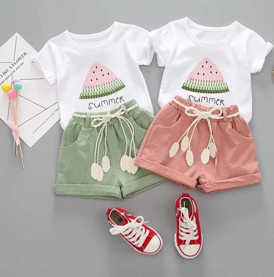 Two girls' outfits with white watermelon-print T-shirts and green or pink shorts