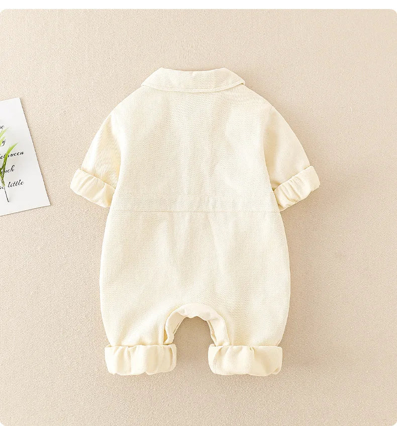 Back of the white baby jumpsuit showing the collar, waist seam, and rolled sleeve and leg cuffs.