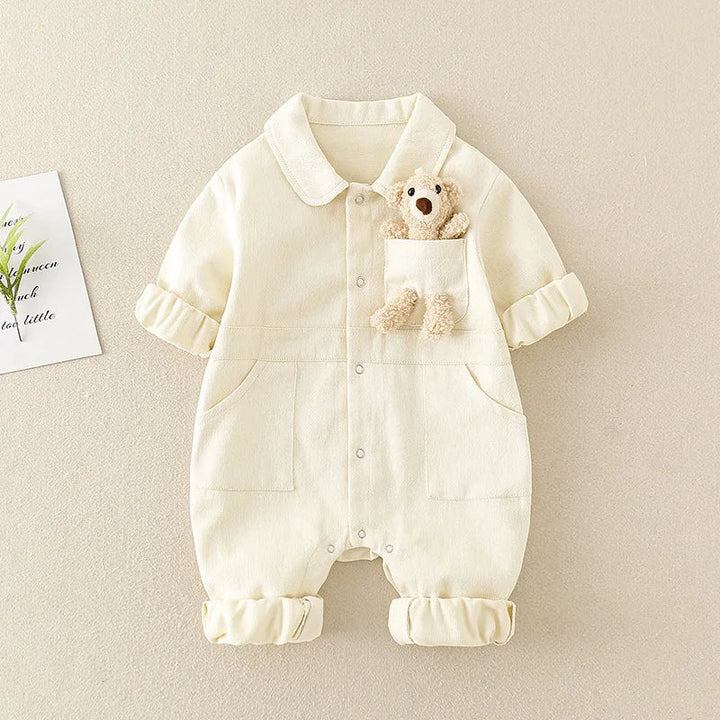 White baby jumpsuit showing the button front, large front pockets, and bear detail at the chest.
