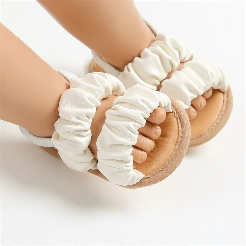 White ruched baby sandals worn on little feet, showing the open-toe design