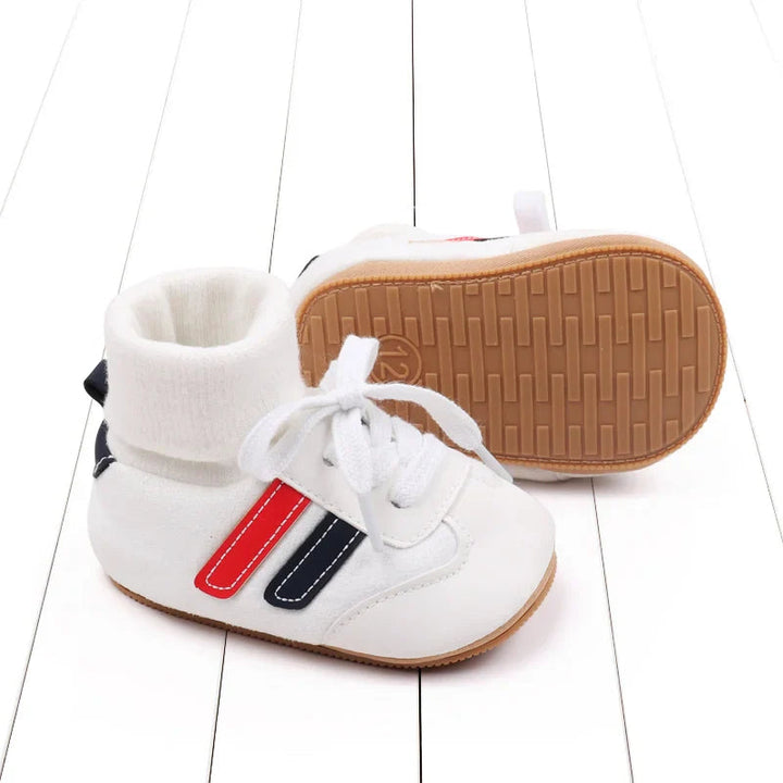 White baby shoes showing red and navy side stripes and a textured tan sole