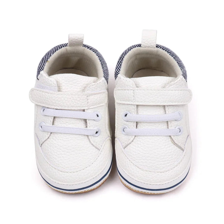 White baby sneakers viewed from the front, showing straps, lace detailing, and striped collars