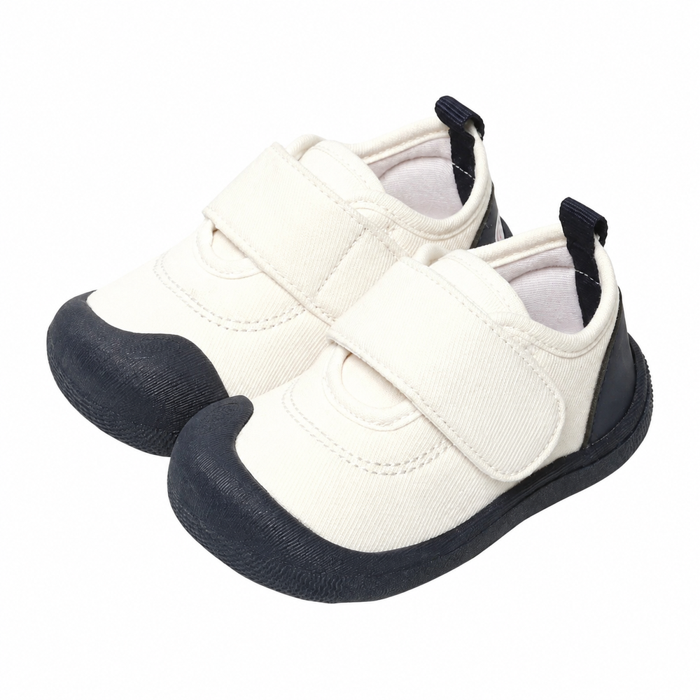 White canvas baby sneakers with black toe caps, black soles, and wide strap closures