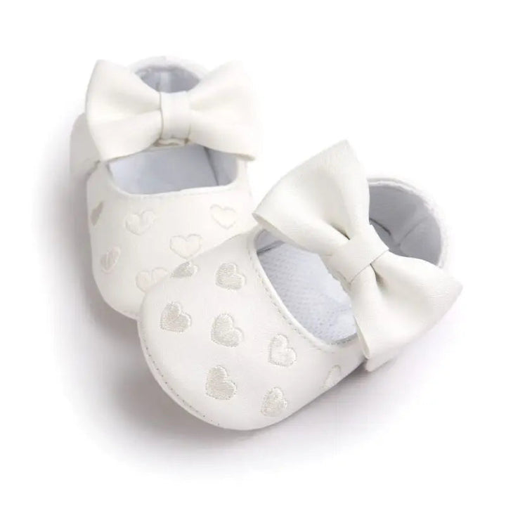White bow baby shoes with heart details, arranged at an angle