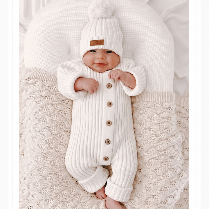 Baby in a white ribbed button-front romper resting on a pale knitted blanket