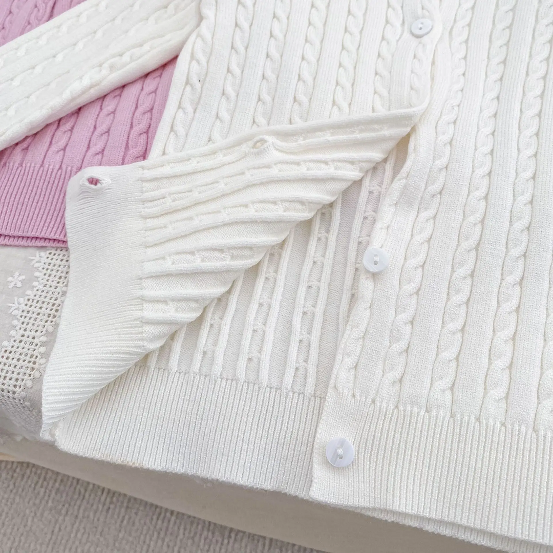 White cardigan with a folded sleeve showing cable-knit texture, front buttons, and a ribbed hem