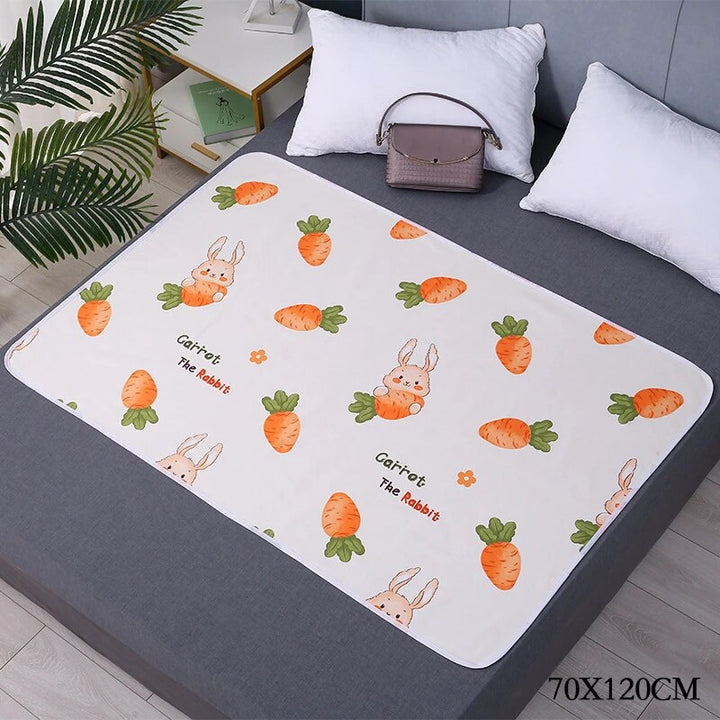 White changing mat with orange carrots and bunnies on a gray bed, labeled 70 x 120 cm.