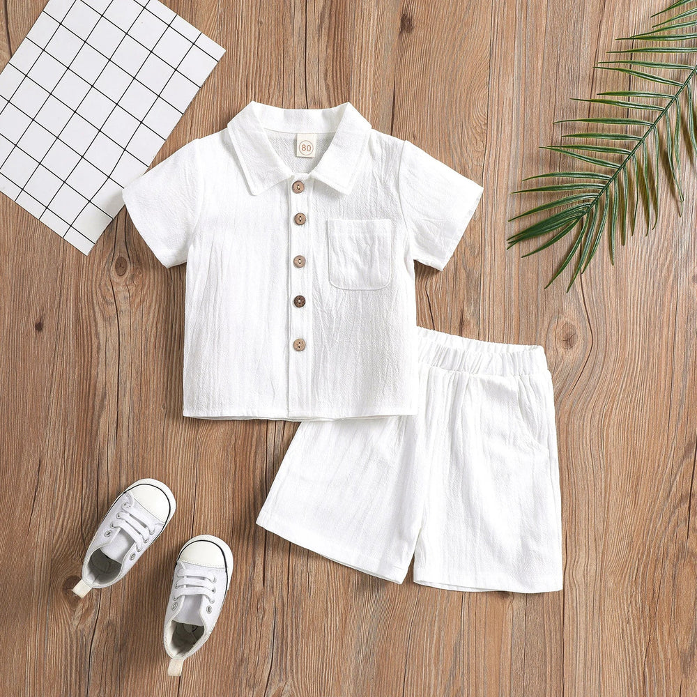 White cotton baby outfit with a button-front shirt, chest pocket, and matching elastic-waist shorts
