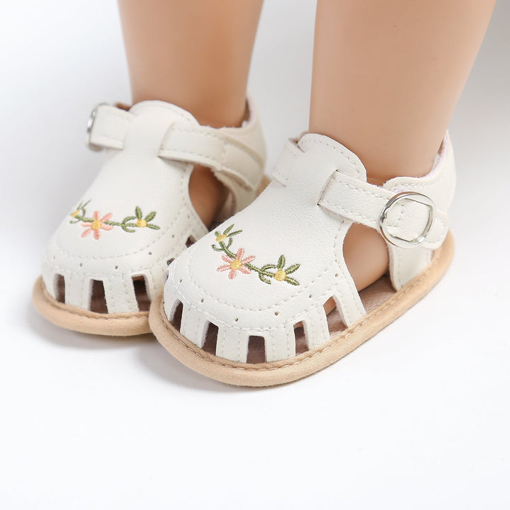 White baby sandals shown from the front with flower embroidery and adjustable straps
