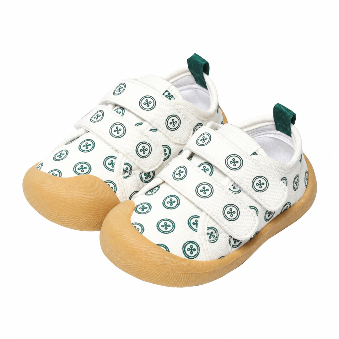 White baby sneakers with green circular prints, strap closures, and tan soles