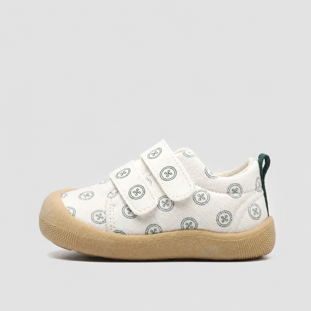 Side view of a white canvas sneaker with green circular prints and a tan sole