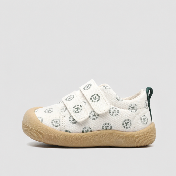 Side view of a white canvas sneaker with green circular prints and a tan sole