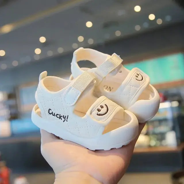 Side view of white sandals with strap closures, open sides and smiley-face details.