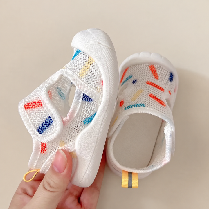 A white printed mesh sandal flexed by hand, with its hook-and-loop strap open