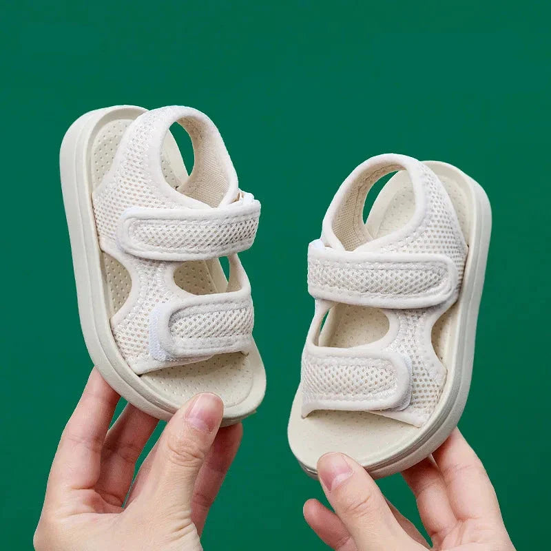 Front view of white kids' sandals held against a green background