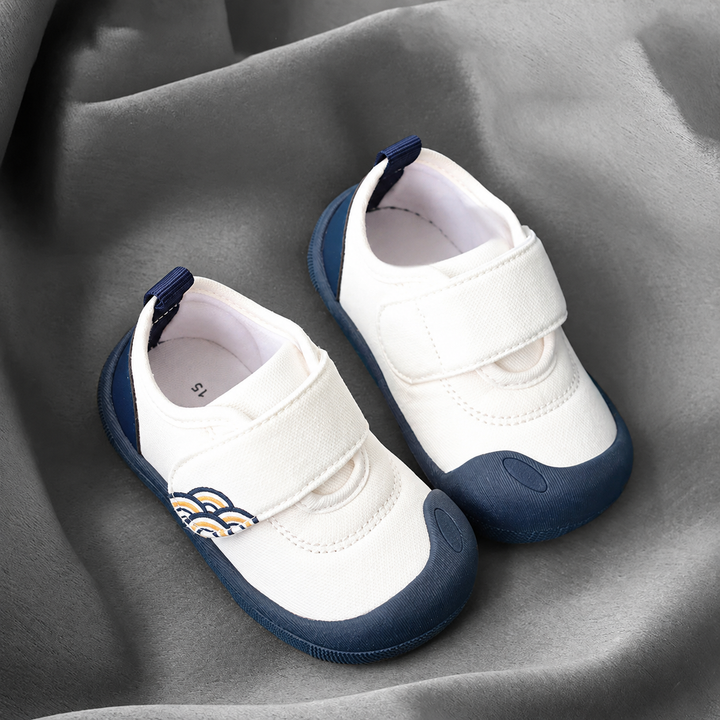 Pair of white baby sneakers with navy toe caps, navy soles, and wide strap closures