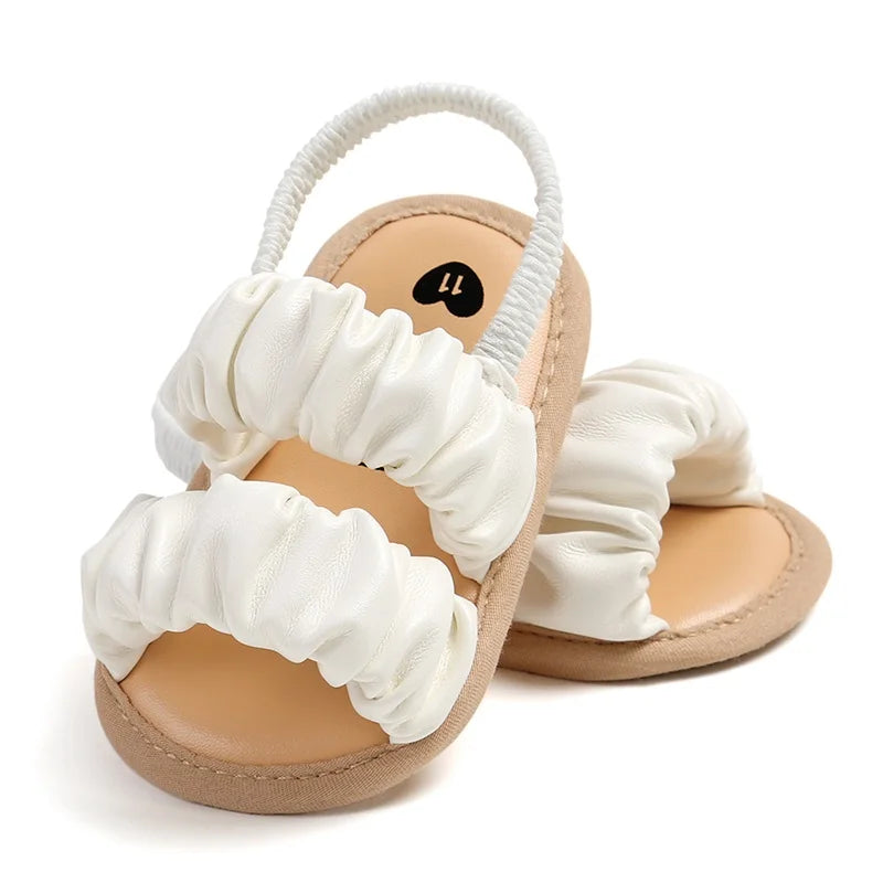 White ruched baby sandals arranged upright to show the open toes and heel straps
