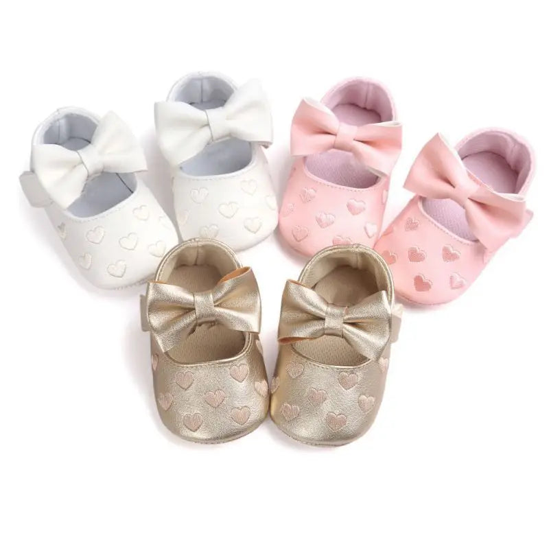 White, pink, and gold bow baby shoes arranged in three pairs