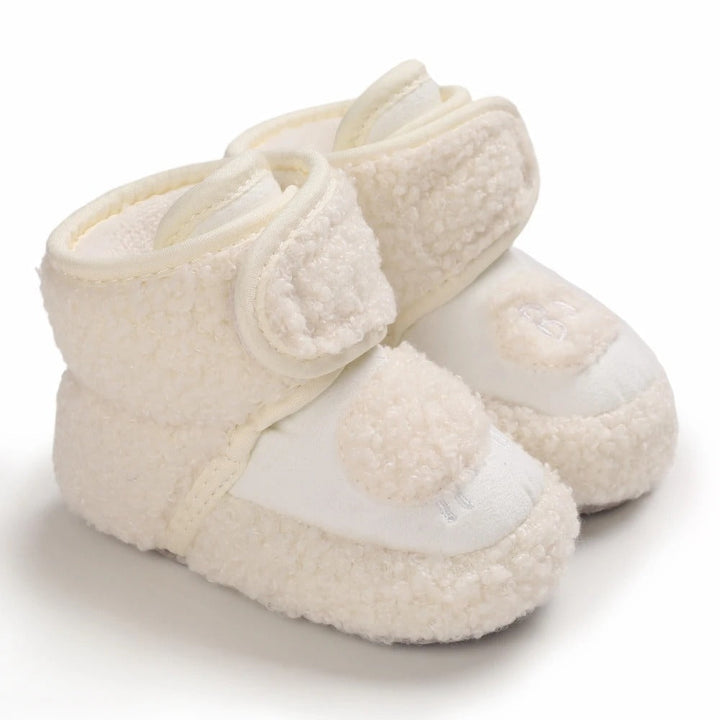 White plush baby shoes with round fuzzy toe accents and ankle straps.