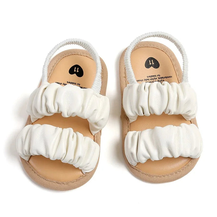 White baby sandals with two ruched front straps and elastic heel straps, viewed from above