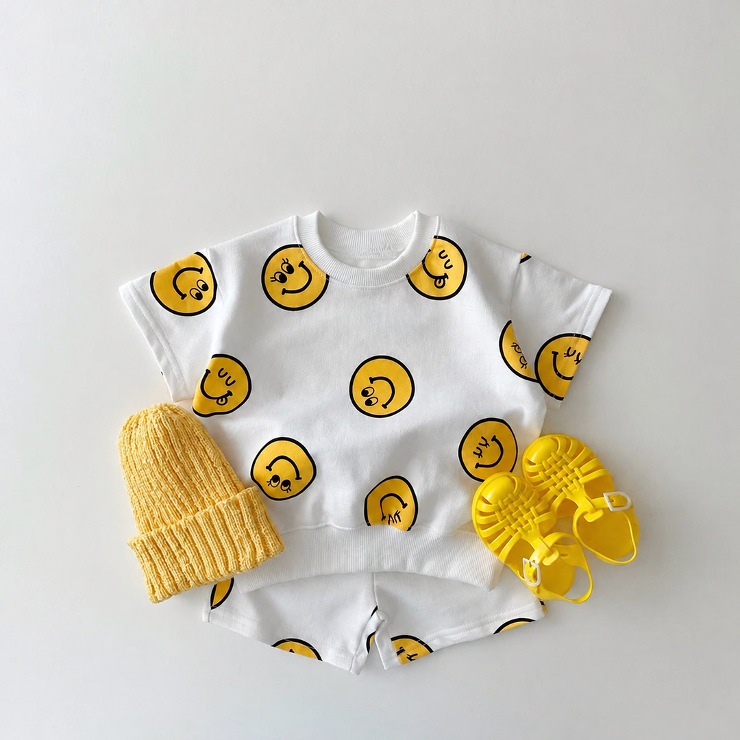 White smiley-print T-shirt and shorts set styled with a yellow knit hat and yellow sandals