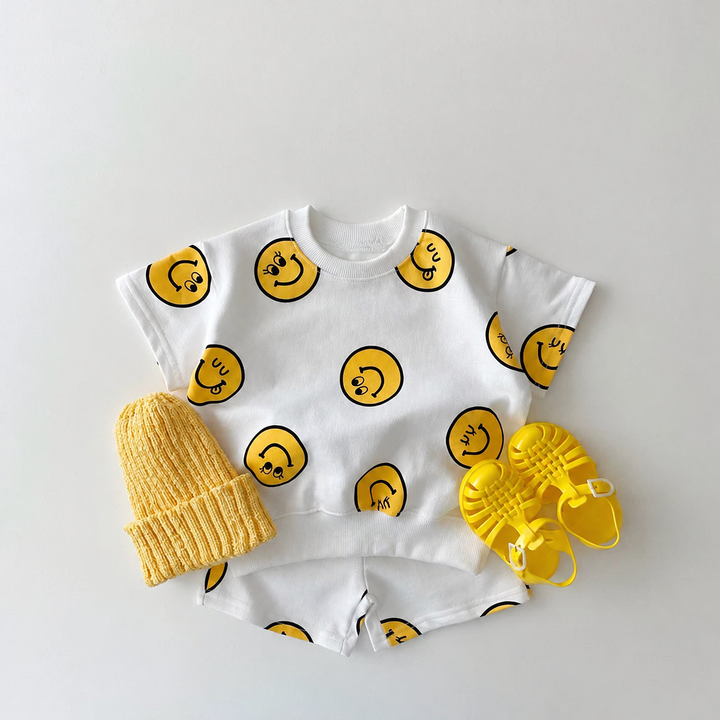 White smiley-print T-shirt and shorts set styled with a yellow knit hat and yellow sandals