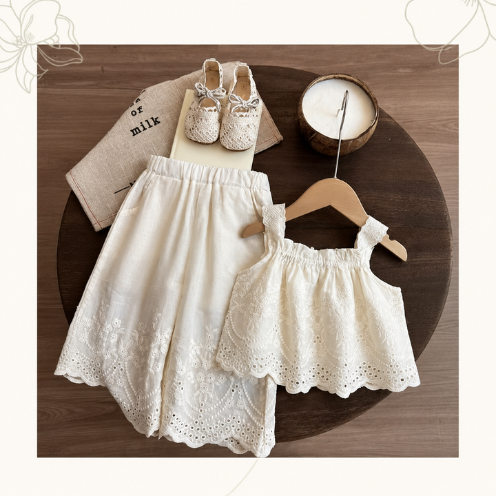 White lace top and matching wide-leg pants arranged on a round table within a decorative border