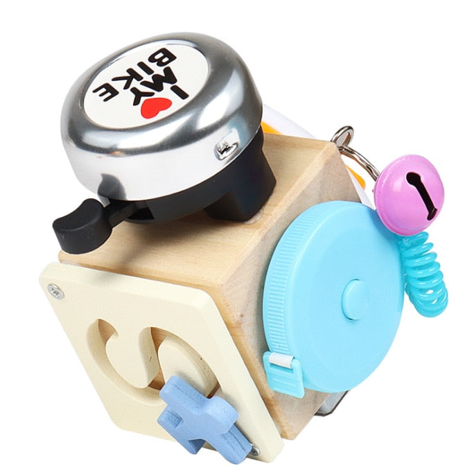 Wooden activity cube with a bicycle bell, blue dial, and pink bell