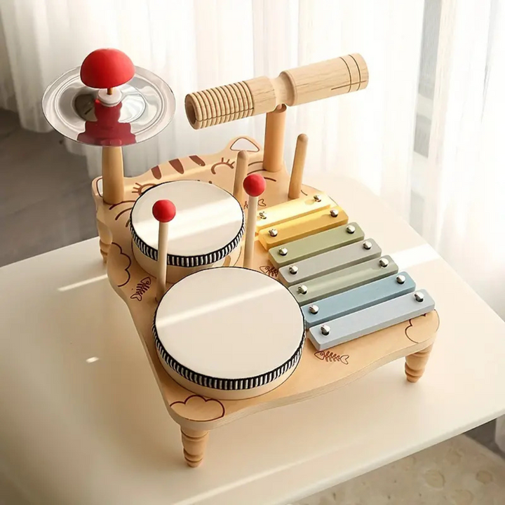 Wooden drum set on a white table with two drums, a pastel xylophone, and a cymbal