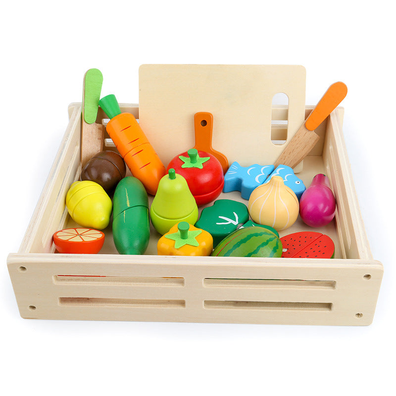 Wooden crate filled with colorful play fruits, vegetables and fish, with a cutting board and utensils