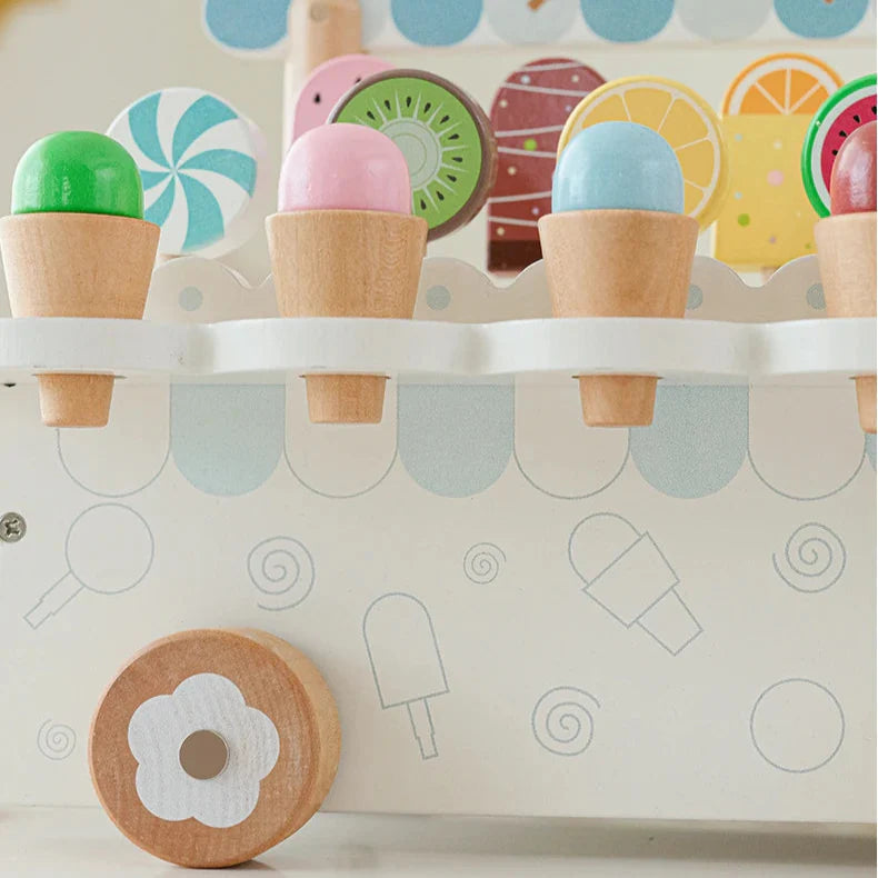 Close-up of colorful wooden ice cream cones in display slots above a flower-centered cart wheel