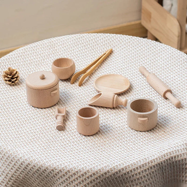 Wooden pot, cups, scoops, tongs and rolling pin arranged on a textured tablecloth.