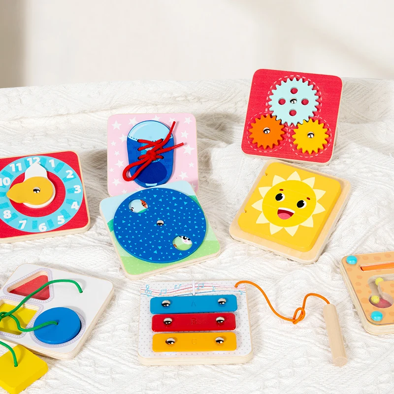 Wooden activity boards arranged on a quilt with lacing, gears, a clock, a mirror, and a tap piano.